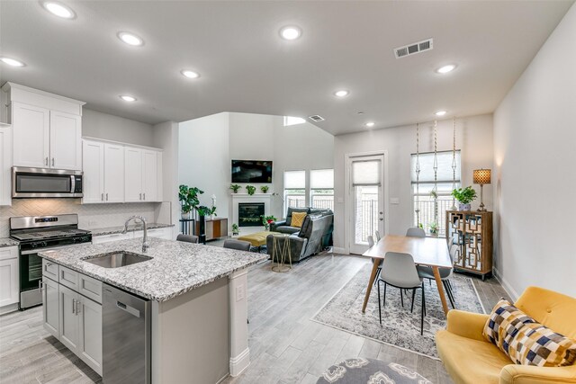 kitchen featuring light wood finished floors, a sink, visible vents, an island with sink, and appliances with stainless steel finishes