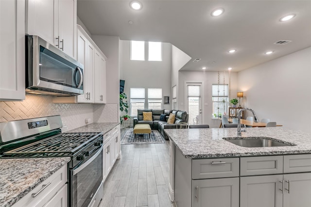 kitchen featuring stainless steel appliances, visible vents, a sink, light wood-type flooring, and decorative backsplash