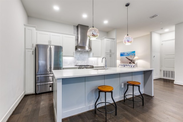kitchen with a sink, freestanding refrigerator, backsplash, wall chimney range hood, and dark wood-type flooring
