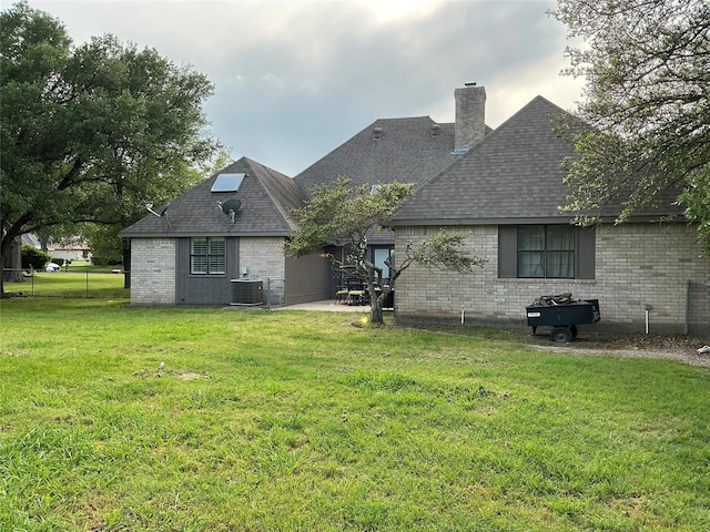1302 Summit Dr, Mexia, TX 76667 - rear view of house with central air condition unit, a chimney, a lawn, a shingled roof, and brick siding