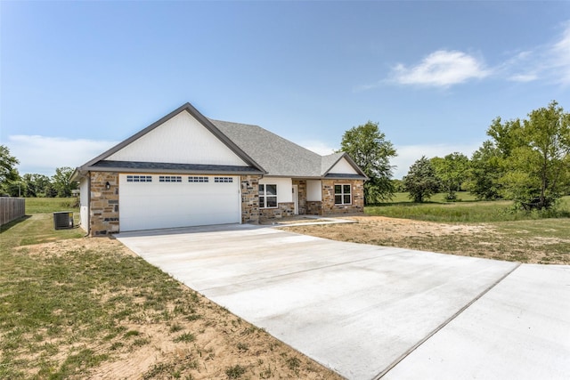 craftsman-style house with an attached garage, a front lawn, stone siding, central AC unit, and driveway