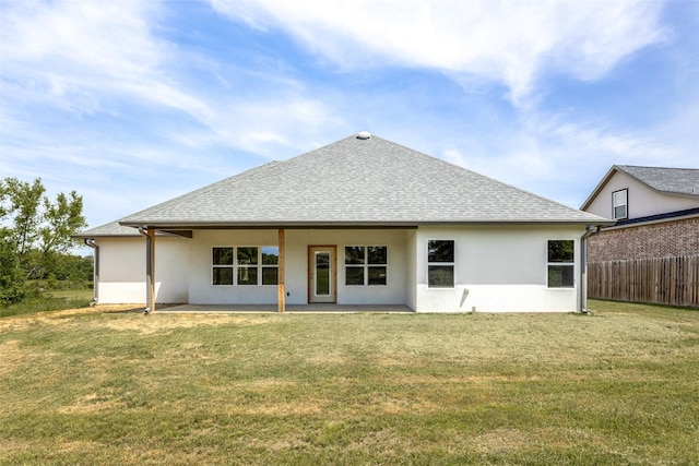 rear view of property with roof with shingles, fence, stucco siding, and a yard