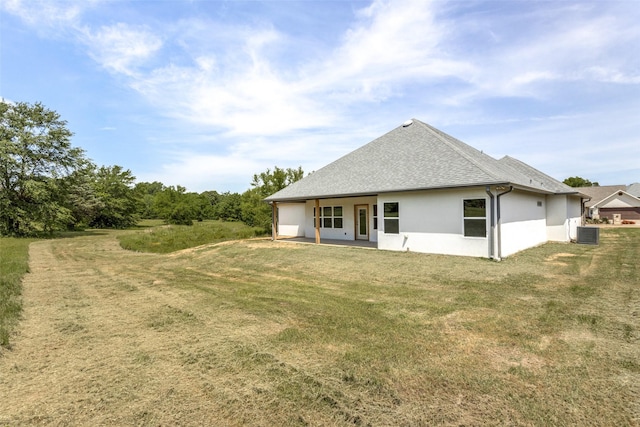 rear view of house featuring a lawn, central AC unit, stucco siding, and roof with shingles
