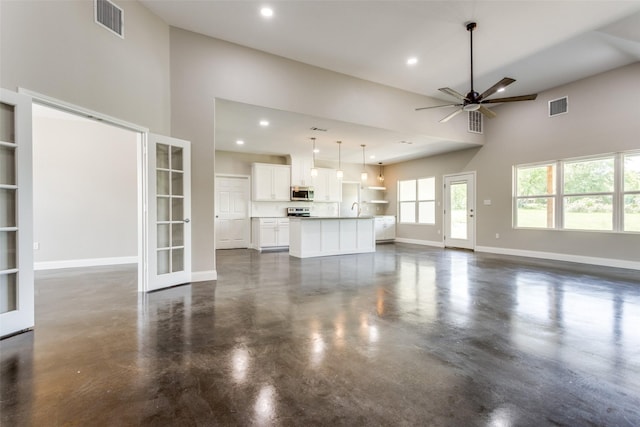 unfurnished living room featuring ceiling fan, visible vents, concrete floors, and a towering ceiling
