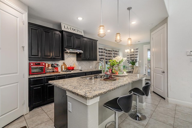 kitchen featuring a sink, stainless steel gas cooktop, dark cabinetry, light tile patterned floors, and tasteful backsplash