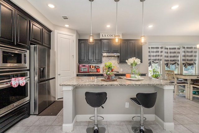 kitchen with under cabinet range hood, stainless steel appliances, visible vents, and a kitchen breakfast bar