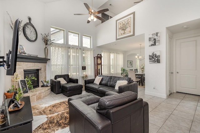 living room featuring a stone fireplace, light tile patterned floors, high vaulted ceiling, baseboards, and ceiling fan with notable chandelier