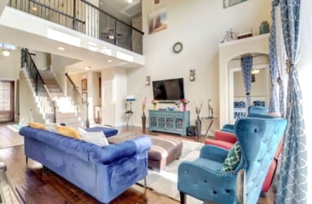 living room with stairs, baseboards, a towering ceiling, arched walkways, and wood finished floors