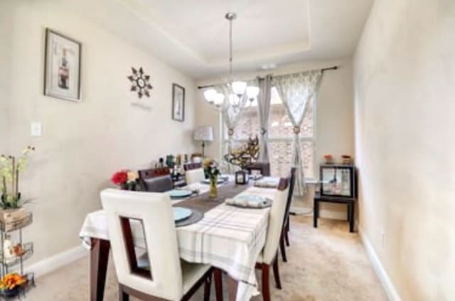 dining room featuring baseboards, light carpet, a chandelier, and a raised ceiling