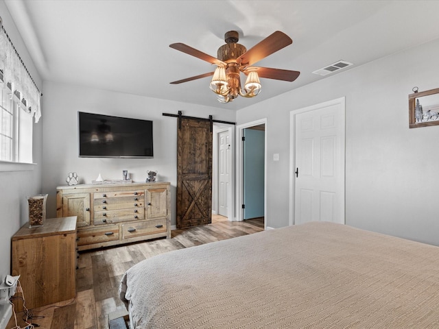 bedroom featuring a ceiling fan, visible vents, a barn door, and wood finished floors