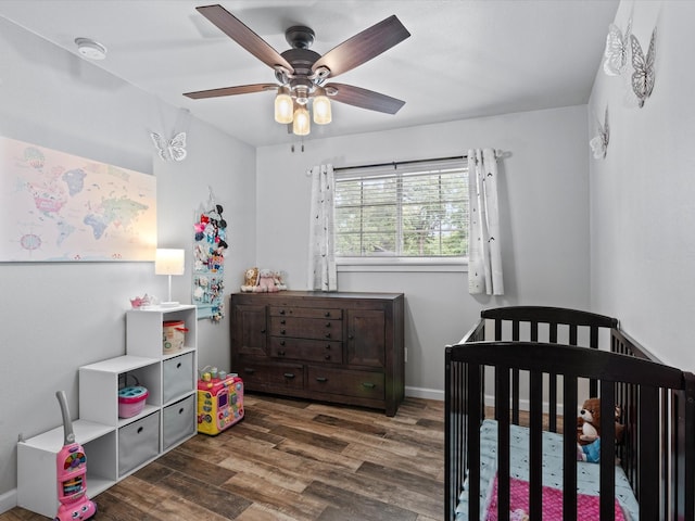 bedroom with a nursery area, a ceiling fan, and wood finished floors