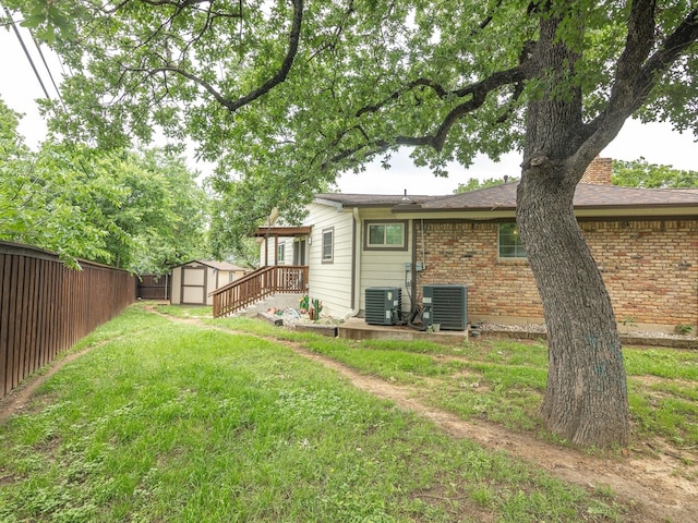 view of yard with an outdoor structure, fence, central AC unit, and a shed