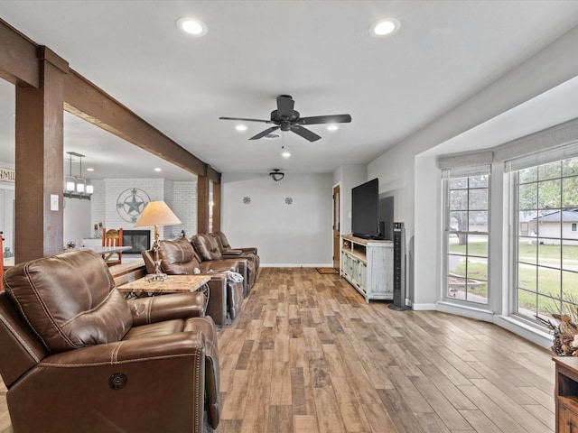 living room with baseboards, ceiling fan with notable chandelier, light wood finished floors, and a fireplace