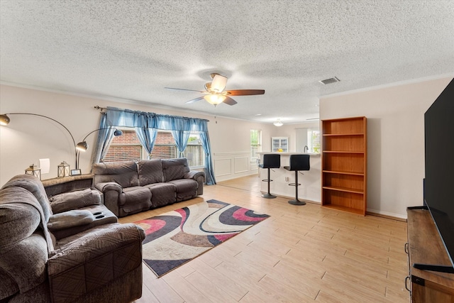 living room featuring light wood-type flooring, a ceiling fan, visible vents, and a textured ceiling