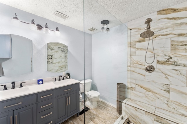bathroom with toilet, visible vents, a sink, and a tile shower