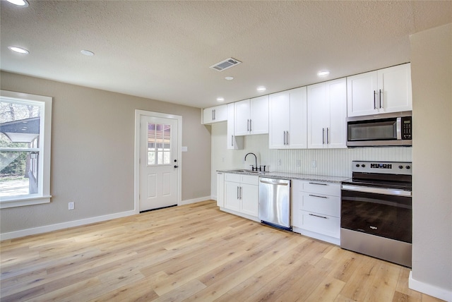kitchen with light stone counters, light wood-style floors, stainless steel appliances, and a sink