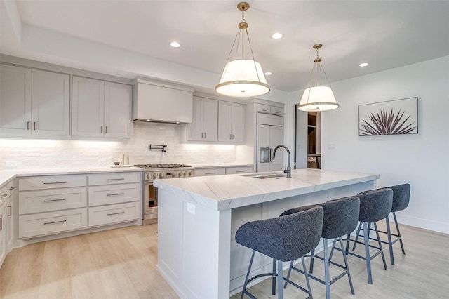 kitchen featuring a sink, tasteful backsplash, light wood-style floors, high end appliances, and light stone countertops