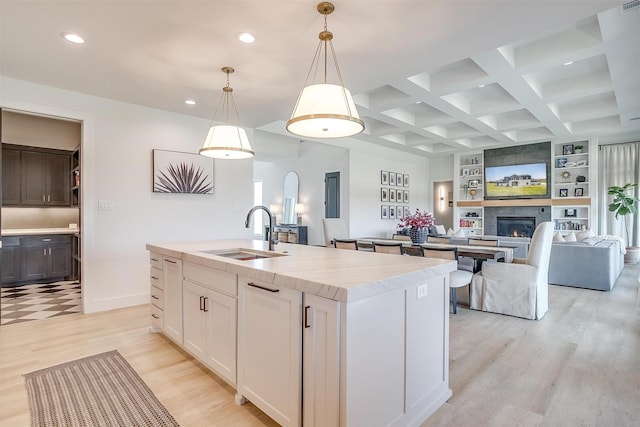 kitchen featuring an island with sink, a glass covered fireplace, a sink, and recessed lighting
