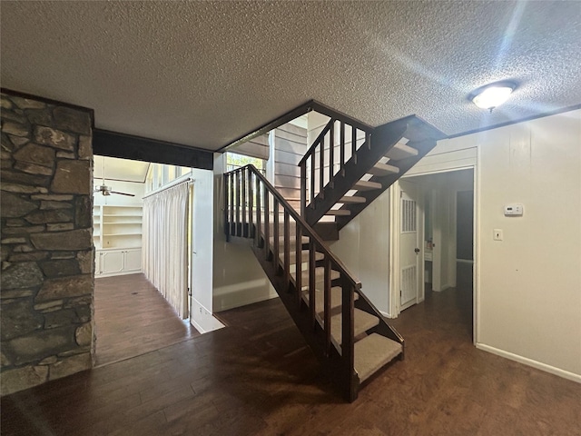 stairway with wood finished floors, a textured ceiling, and baseboards