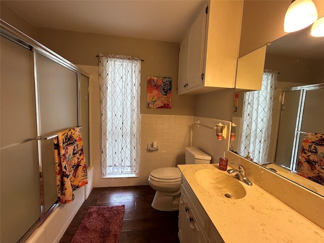 bathroom featuring toilet, wainscoting, tile walls, vanity, and enclosed tub / shower combo