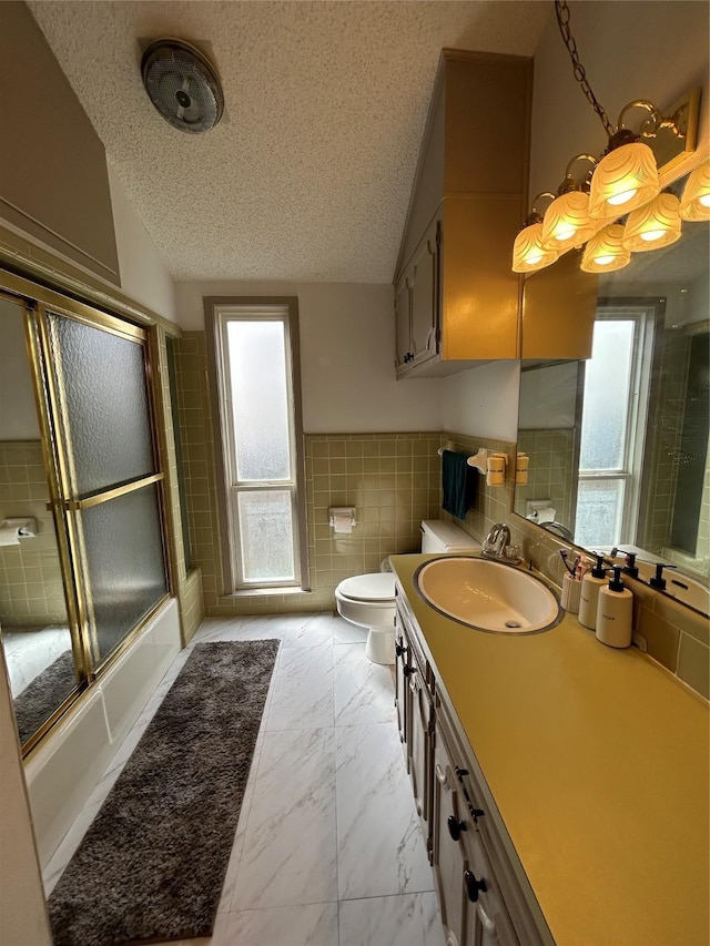 full bathroom with tile walls, plenty of natural light, vanity, and a textured ceiling