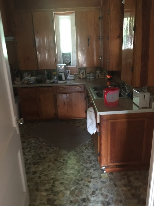 kitchen with tile patterned floors, light countertops, a sink, a peninsula, and brown cabinetry