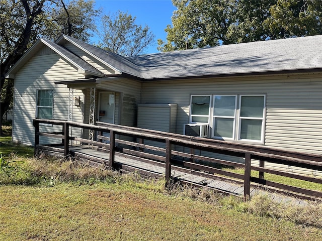 rear view of property with a lawn, a wooden deck, cooling unit, and a shingled roof