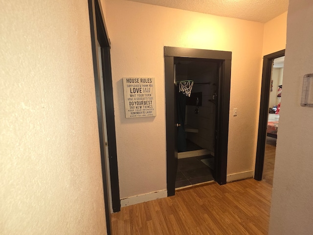 hall featuring wood finished floors, a textured ceiling, and baseboards