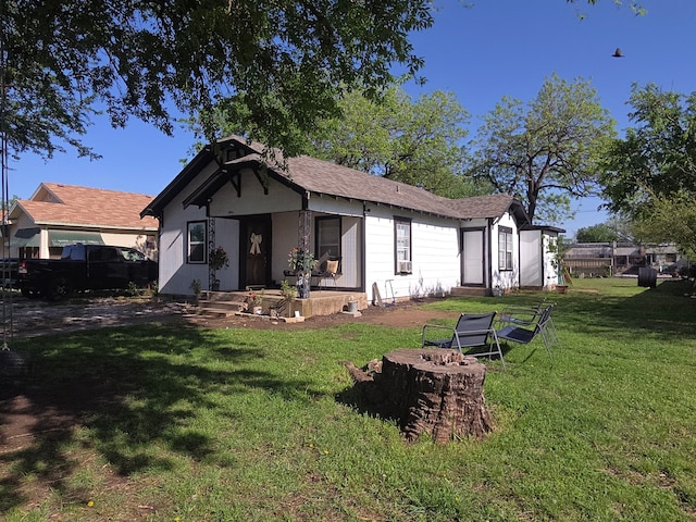 back of property with a lawn, fence, roof with shingles, and an outdoor fire pit