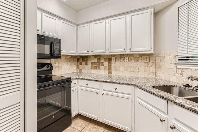 kitchen with white cabinets, light tile patterned flooring, light stone counters, and black appliances