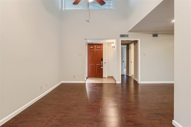 empty room featuring visible vents, a ceiling fan, a towering ceiling, and wood finished floors