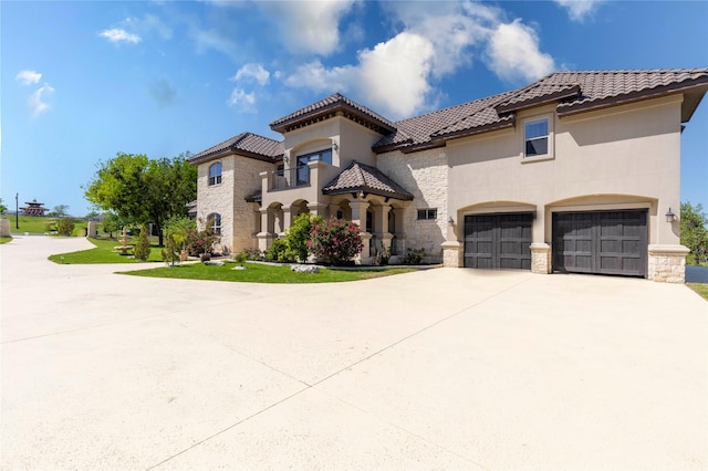 mediterranean / spanish-style home featuring stone siding, a tile roof, stucco siding, and concrete driveway