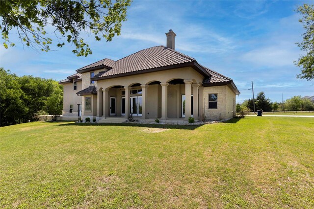 back of property featuring a lawn, a tiled roof, a chimney, and stucco siding
