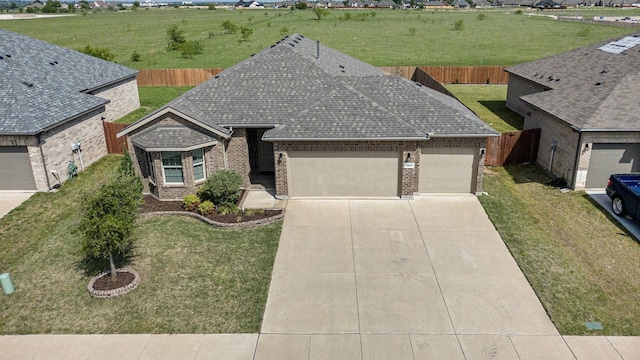 view of front of home featuring driveway, fence, brick siding, an attached garage, and a shingled roof