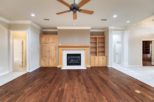 unfurnished living room featuring wood finished floors, a tiled fireplace, visible vents, and a ceiling fan