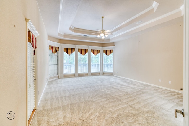 carpeted empty room with a raised ceiling, a ceiling fan, baseboards, and ornamental molding