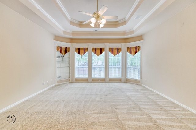 empty room featuring a ceiling fan, light carpet, a tray ceiling, baseboards, and ornamental molding