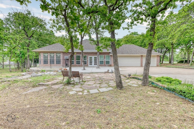 rear view of house with french doors, roof with shingles, concrete driveway, brick siding, and an attached garage