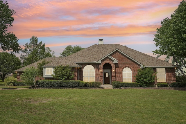 ranch-style house with a lawn, roof with shingles, a chimney, and brick siding
