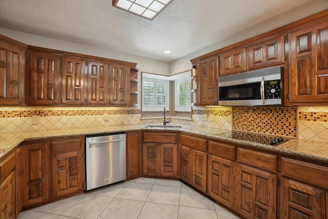 kitchen featuring light stone counters, a textured ceiling, a sink, light tile patterned flooring, and stainless steel appliances