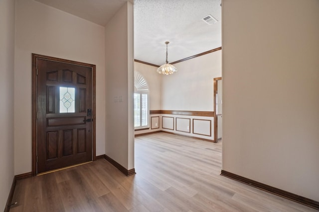 entrance foyer featuring a wainscoted wall, baseboards, visible vents, an inviting chandelier, and light wood-style floors