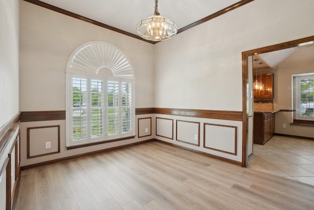 empty room with wainscoting, an inviting chandelier, ornamental molding, and light wood finished floors