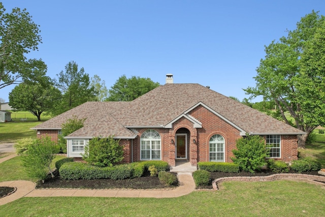 ranch-style home featuring a chimney, a front lawn, brick siding, and a shingled roof