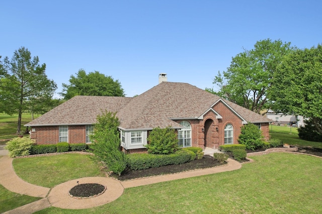 ranch-style home featuring a chimney, brick siding, roof with shingles, and a front yard