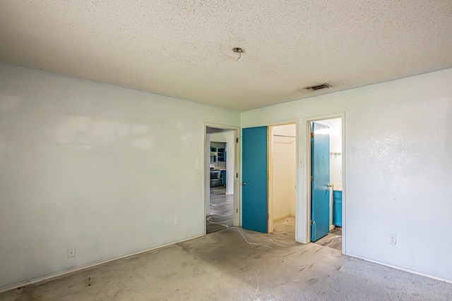 unfurnished bedroom with a walk in closet, carpet flooring, a textured ceiling, and visible vents