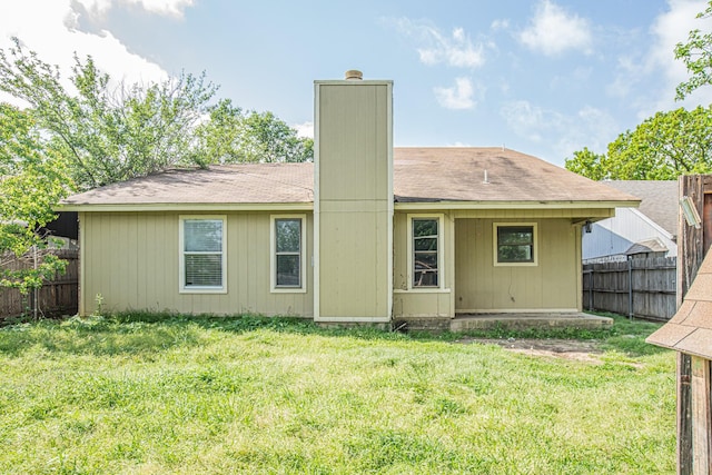 rear view of house featuring a chimney, fence, and a lawn