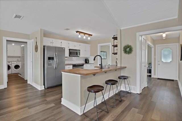 kitchen featuring a peninsula, washer and clothes dryer, visible vents, wooden counters, and appliances with stainless steel finishes