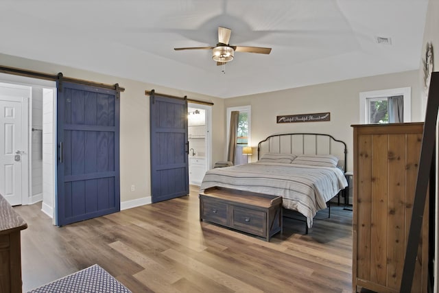 bedroom featuring a barn door, a ceiling fan, wood finished floors, baseboards, and visible vents