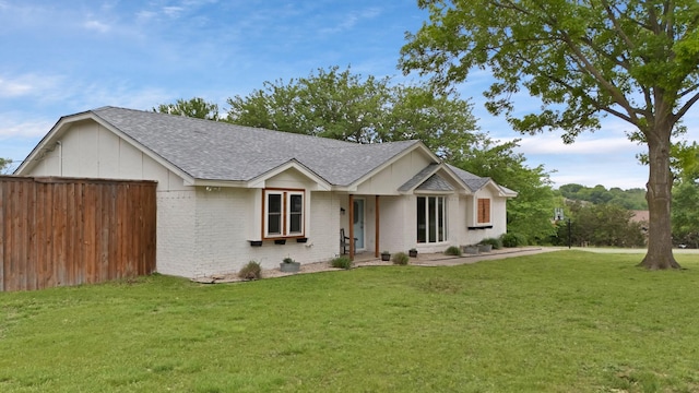 single story home with an attached garage, a shingled roof, a front lawn, and brick siding