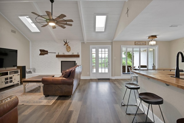 living room with vaulted ceiling with skylight, ceiling fan, a brick fireplace, dark wood-type flooring, and visible vents